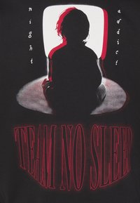 Camiseta de tela negra con un diseño gráfico de una figura en silueta sentada frente a una pantalla luminosa, con el texto "TEAM NO SLEEP" en negrita y color rojo.