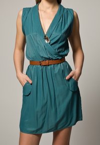 Teal dress with a wrap design, sleeveless, featuring a brown belt. Includes two front pockets and smooth, lightweight fabric.