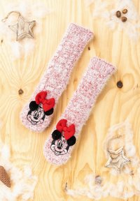 Calze rosa pelose con ricamo di Minnie Mouse, caratterizzate da un fiocco rosso e dettagli neri, su uno sfondo di legno con elementi decorativi.