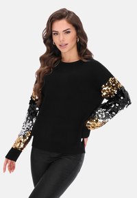 Schwarzer Pullover mit langen Ärmeln, verziert mit goldenen und silbernen Pailletten. Weiches Material, rundhalsausschnitt und enganliegende Bündchen.