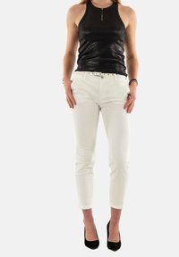 Top negro sin mangas con una textura brillante, combinado con pantalones blancos ajustados y zapatos de tacón negros. Diseño simple con un cinturón en los pantalones.