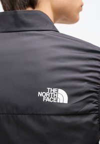 Άτομο που φοράει μαύρο μπουφάν με το λογότυπο The North Face στην πλάτη, γυρισμένο πλάτη στην κάμερα.