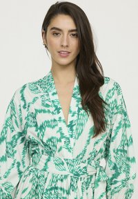 Kimono vert et blanc à motifs avec une taille à nouer, doté d'un tissu texturé et de larges manches, conçu dans une coupe ample et fluide.