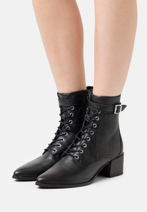 Botines negros hechos de cuero texturizado, con punta afilada, cordones en la parte delantera y una correa con hebilla en el tobillo. Diseño de tacón cuadrado.