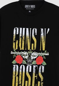 Maglietta nera con la scritta "GUNS N' ROSES" in bianco e giallo logorato, accompagnata da un'immagine di un revolver e rose rosse. Taglia XL.
