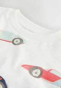 Material alb cu ilustrații imprimate de mașini vintage în nuanțe de albastru deschis, roșu și albastru închis, prezentând un guler rotund cu dungi.