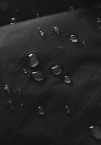 Schwarzer Stoff mit strukturierter Oberfläche, der mit mehreren Wassertropfen unterschiedlicher Größen bedeckt ist, was seine wasserabweisenden Eigenschaften hervorhebt.