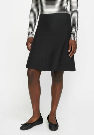 Jupe évasée noire en tissu texturé, longueur genou, associée à un haut à manches longues noir et blanc rayé et des ballerines noires.