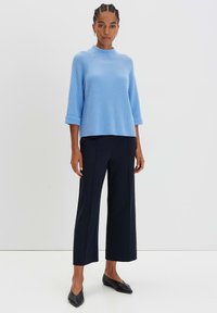 Helles blaues, geripptes Sweatshirt mit hohem Kragen und Dreiviertelärmeln, kombiniert mit weit geschnittenen marineblauen Hosen und schwarzen Ballerinas.