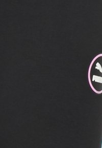 Svart tyg t-shirt med en rund logga med rosa kant. Loggan visar en hoppande puma och ordet "PUMA" i vitt.