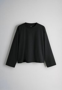 Black long-sleeve crew neck shirt hanging against a plain light gray background.