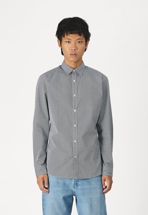 Camisa de botones de manga larga en color azul marino con un patrón geométrico blanco, que presenta un collar de punta y un dobladillo recto. Combinada con jeans de color azul claro.