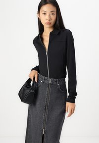 Juodas zip-up viršus su apykakle, derinamas su pilku džinsiniu sijonu aukštu liemeniu, turinčiu priekinį užtrauktuką. Modelis laiko mažą juodą rankinę.