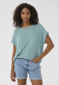 Hellblauses, lockeres Oberteil mit kurzen Ärmeln, strukturierter Stoff, kombiniert mit Denim-Shorts mit umgeschlagenen Säumen. Einfaches und lässiges Design.