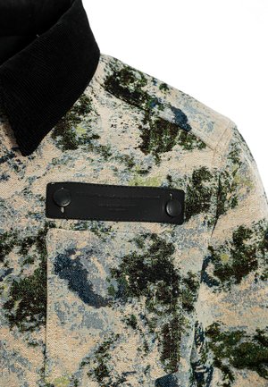 Americana con cuello en tejido texturizado con un patrón botánico en verdes y azules, que presenta un bolsillo de parche negro y botones.