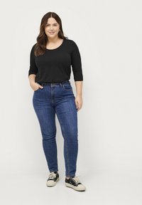 Top negro de manga larga combinado con jeans ajustados de color azul oscuro. El modelo lleva zapatillas negras y blancas. Look sencillo y casual.