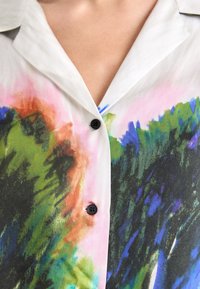Kortärmad skjorta i lätt tyg, med ett färgglatt abstrakt mönster av grönt, blått och rosa, med svarta knappar och en spetsig krage.