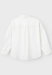 Camicia bianca a maniche lunghe, realizzata in tessuto leggero, presenta un plissé sul retro, colletto e polsini abbottonati. Texture liscia, design minimale.