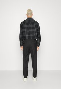 Camicia a scacchi bianca e nera con maniche lunghe abbinata a pantaloni neri. Tessuto visibilmente liscio e taglio strutturato. Calzature informali.