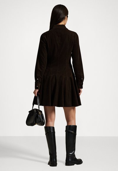 Brown corduroy shirt dress with a flared hem, long sleeves, and buttoned cuffs; paired with black knee-high boots and a small black bag.