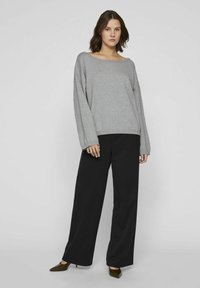 Grijze oversized sweater met een brede halslijn, gecombineerd met zwarte wijde broekspijpen. Glad materiaal en een relaxte pasvorm. puntige schoenen.