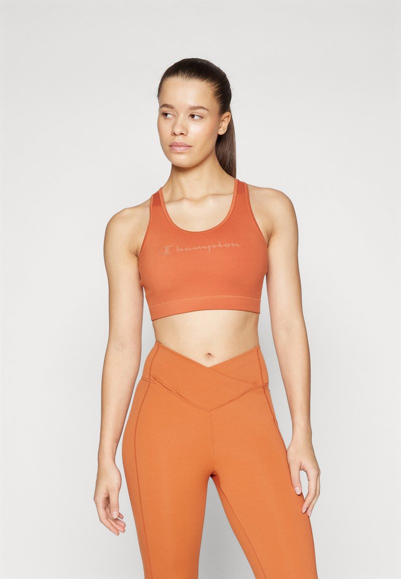 Oransje sports-bh med rund hals og Champion-logo, kombinert med matchende høy midje leggings med en vinklet design.