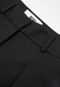 Zwarte broek van gestructureerde stof, met een platte voorkant, scherpe plooien en een label met de tekst "BENH." Zichtbare zakken en een gestructureerd ontwerp.