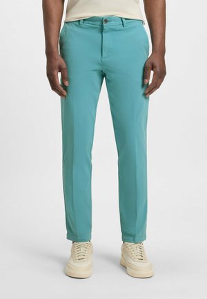 Turquoise trousers made from a lightweight fabric, featuring a front button closure, flat front, and side pockets, paired with beige sneakers.