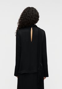 Μαύρο τοπ με μακριά μανίκια και άνοιγμα στην πλάτη σε σχήμα κλειδιού, με ρευστή σχεδίαση, λεία υφή και διακοσμητικό κασκόλ με φούντες.