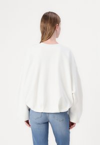 Fehér, oversize pulóver kerek nyakkal, ejtett vállakkal és sima textúrával, világoskék, testhezálló farmernadrággal párosítva.