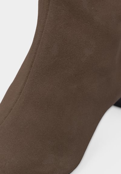 Κοντινή φωτογραφία καφέ δερμάτινου παπουτσιού με τακούνι, παρουσιάζοντας ομαλή υφή και στρογγυλεμένη μύτη με ελαφρώς καμπυλωτό τακούνι.