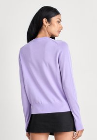 Lila pullovertröja med långa ärmar, ribbad nederkant och rund halsringning. Slät textur med minimala sömmar. Bärs över en svart kjol.