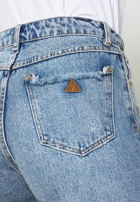 Ljusblå denimjeans med slitna detaljer, featuring en triangulär läderlapp på bakfickan och en strukturerad midja.