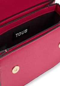 Cartera de cuero texturizado en color rosa con acentos de hardware dorado. El interior cuenta con compartimentos y una etiqueta de marca visible "TOUS."