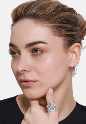 Silberner Statement-Ring mit einem unregelmäßigen, skulpturalen Design. Trägt man am Daumen, wodurch eine polierte, reflektierende Oberfläche auf der Haut hervorgehoben wird.