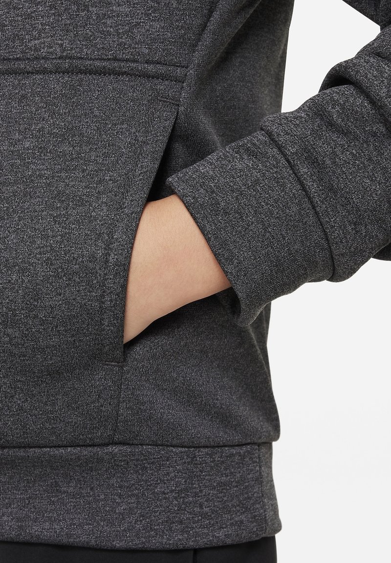 Felpa grigio scuro con tessuto strutturato, dotata di una tasca frontale e polsini a costine. Primo piano sulla manica e sulla mano nella tasca.