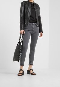 Chaqueta de cuero negra, camiseta negra, jeans ajustados grises, sandalias de tacón bloque negro y un bolso de tote negro texturizado con detalles troquelados.