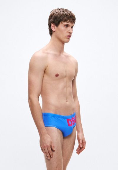 Erksamalt sinised ujumispüksid, mis sobivad tihedalt ja millel on esiküljel julge roosa "DSG" logo. Sile tekstuur ega nähtavaid kinnitusi pole.