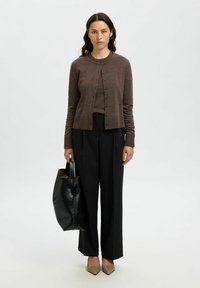 Cardigan marrone, con bottoni davanti, abbinato a una maglia marrone e pantaloni neri a gamba larga. Borsa nera con forma arrotondata e dettagli tan.