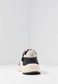 Černé a béžové sportovní tenisky s texturovaným černým panelem, světlým semišovým podpatkem a logem na podešvi. Obsahují poutko.