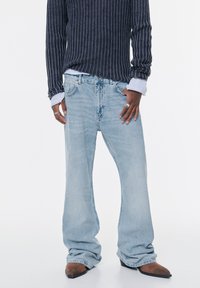 Svijetloplave traperice širokog kroja, izblijedjele teksture i opuštenog stila, kombinirane s tamnim rebrastim puloverom i smeškim čizmama na špic.