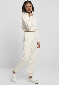 Kremfarget, tettsittende hettegenser med kengurulomme og matchende joggebukser. Mykt, teksturert stoff; elastiske mansjetter og midjebånd; hvite sneakers.