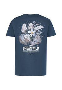Navyblauwe T-shirt met een witte bloem die door gebroken beton groeit en de tekst "Urban Wild" op de achterkant.