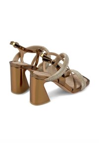Sandales à talons hauts en bronze avec des lanières croisées, ornées d'accents scintillants et d'un talon géométrique épais. Texture brillante en vernis.