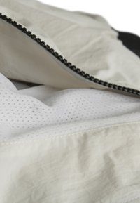 Vit tyg med en texturerad yta, försett med en ventilationsnät och en kontrasterande svart dragkedja längs kanten.