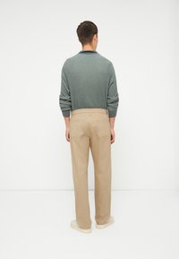 Cămașă lungă cu mânecă lungă, de culoare verde deschis, cu o textură riglasă, asociată cu pantaloni drepți bej. Pantalonii au două buzunare la spate. Textură netedă, croială lejeră.