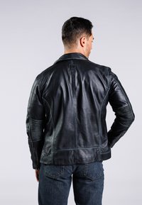 Giubbotto in pelle nera con collo, dettagli cuciti e inserti a coste sulle maniche. Indossato sopra jeans di denim blu.