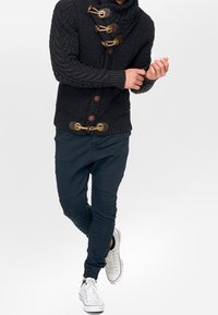 Czarny dziany kardigan z wysokim kołnierzem, z drewnianymi zapięciami typu toggle. W zestawieniu z ciemnymi spodniami i białymi sneakersami.