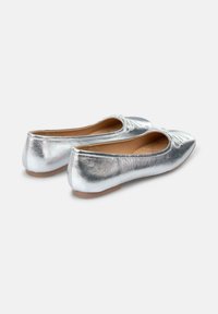 Ballerines métalliques argentées avec une texture lisse, des orteils arrondis et un petit nœud décoratif à l'avant. Semelle en caoutchouc flexible.