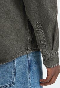 Dunkelgrau denimhemd mit geknöpftem Bund, aus strukturiertem Stoff und mit abgerundetem Saum, kombiniert mit blauen Jeans.